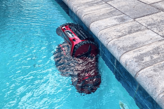 A red robotic pool cleaner working along the edge of a swimming pool