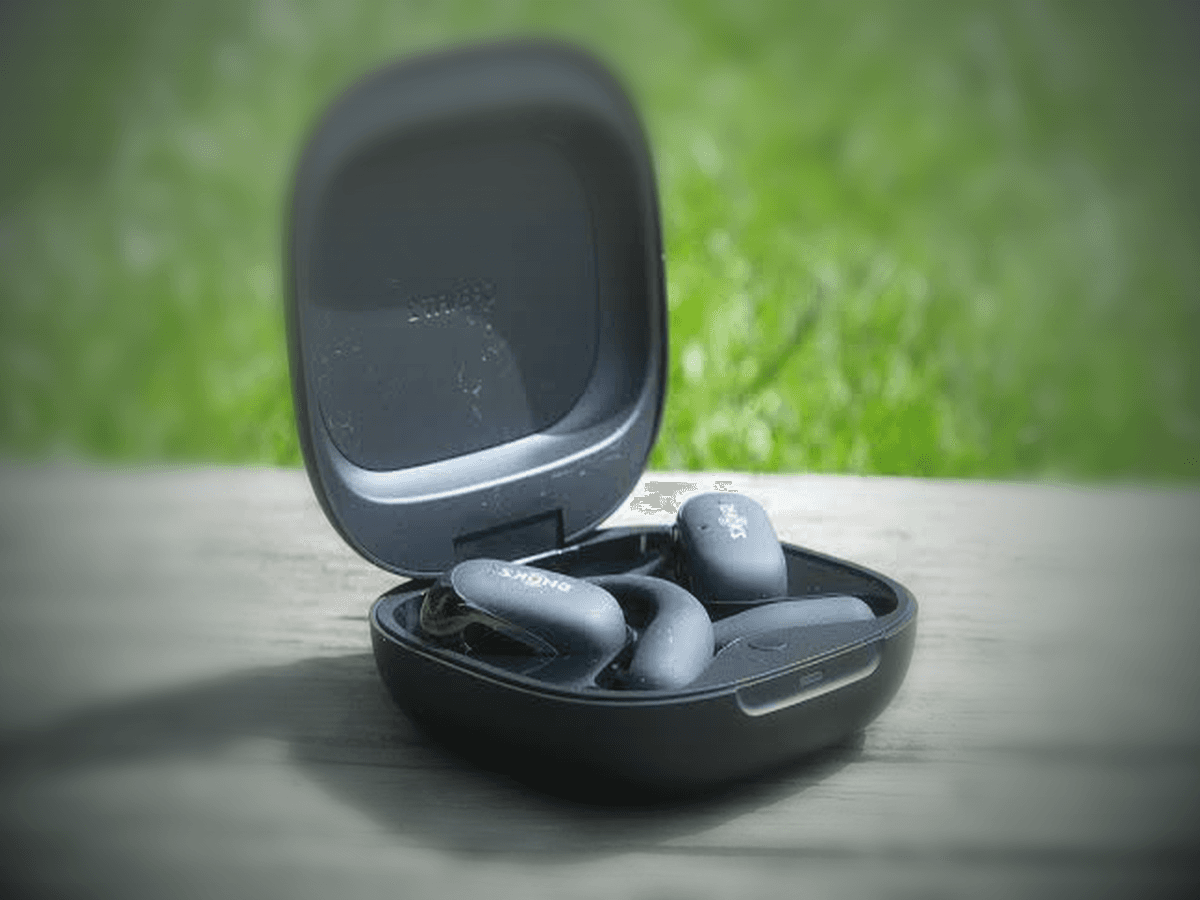 Shokz OpenFit 2 earbuds in an open charging case on a wood surface with soft green background