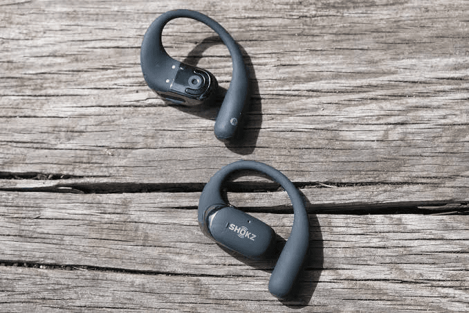 Shokz OpenFit 2 earbuds positioned on a wooden surface to show the open-ear hook shape
